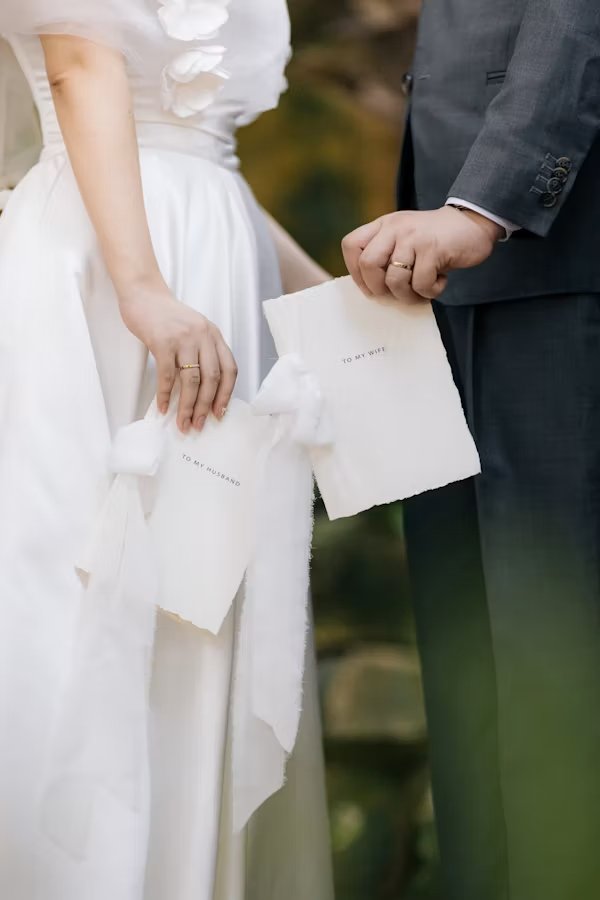 Bruidspaar houdt elkaars handen vast met hun geloften op papier